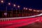 Traces of headlights from cars moving at night on the bridge, illuminated by lanterns. Abstract cityscape with highway at dusk