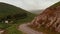 Tracking of car passing through curves around steep rock slope. Road leading in countryside. Ireland