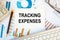 Tracking Expenses is written in a document on the office desk, keyboard and diagram