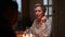 Tracking shot of elegant middle-aged woman sitting at festive table with family and guests, in dark living room with