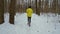 Tracking shot of sporty man running in forest on snow covered path on winter day