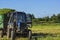 Is a tractor with a body filled with green grass against a background of green meadow and blue sky