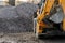 A tractor with a bucket loads stone gravel at a construction site