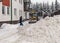 A tractor with a bucket rakes snow into a pile in the yard of the house.