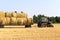 Tractor carrying hay bale rolls - stacking them on pile. Agricultural machine collecting bales of hay on a field