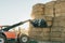 a tractor catching hay bales with a shovel at dawn