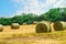 Tractor cutting hay in summer time against blue cloudy sky,  haystacks on the field