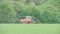 tractor distributing fertilizer on field near forest in slow motion