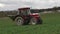 A tractor with a fertilizer spreader turning on a green agricultural field