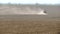 A tractor in a field with a dust cloud behind him