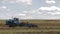 Tractor with harrow system plowing ground on cultivated farm field, pillar of dust trails behind, preparing soil for