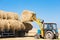 Tractor loading hay bales on truck trailer
