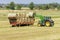 Tractor loading round bales of hay on trailer for transport to destination in the Tuscan countryside, Italy