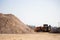 A tractor is loading sand into a truck bed at a construction site. In the foreground - a mountain of sand. reportage