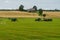 A tractor loads bales of hay onto a trailer from another tractor