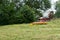 Tractor with mower in front cutting a steep hillside wildflower meadow in the Alps for hay