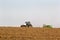 Tractor operates on horizon line ploughed field on foreground