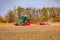 A tractor with a plow on a field in winter creates dust in the blue sky