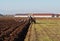 Tractor plows the field in front of some agricultural buildings