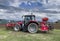 Tractor plows the field in front of some agricultural buildings on a sunny spring day