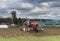 Tractor plows the field in front of some agricultural buildings on a sunny spring day