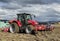 Tractor plows the field in front of some agricultural buildings on a sunny spring day