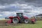 Tractor plows the field in front of some agricultural buildings on a sunny spring day