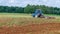 A tractor plows a field, pulling a plow. Agricultural work