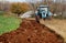 A tractor plows an uncultivated agricultural land for sowing, in the last days of autumn. Alongside there is a green cultivated f