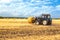 Tractor pulls Round Baler in the background of a field with haystacks