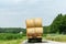 A tractor rides on a road amid fields and carries bales of hay for storage