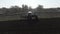 Tractor riding backward along furrows on sundown. Wide shot of agricultural machinery working on rural field on sunset