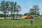 Tractor with silage trailer, freshly mown grassland and road with trees . Farm in the background and fence in the