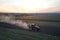 Tractor spraying fertilizers with insecticide herbicide chemicals on agricultural field at sunset