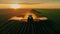 A tractor sprays an agricultural field with fertilizer on a sunset evening. Drone view.