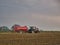A tractor tows a red tanker trailer spraying slurry liquid fertiliser across a cut field of stubble. Taken in Cheshire, UK.