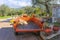 Tractor and trailer with olive rake and pruner parked in Greek village with olive groves on hillside behind