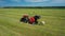 Tractor uses trailed bale machine to collect straw in field and make round large bales. Haymaking. Tractor collecting