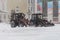 tractors are going to clear the snow in the city. Two tractors with buckets stand side by side during a snowfall.