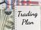 Trading plan written on note book with pen,magnifying glass,compass,money and chart.