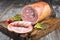 Traditional Allgauer veal roast roll sausage sliced and as piece with tomatoes and chili on an old rustic cutting board