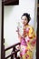 Traditional Asian Japanese beautiful Geisha woman wears kimono hold a fan sit in a summer nature garden