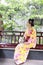 Traditional Asian Japanese beautiful Geisha woman wears kimono sit on a bench in a summer nature garden