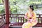 Traditional Asian Japanese beautiful Geisha woman wears kimono sit on a bench in a summer nature garden