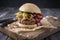 Traditional barbecue Hamburger with gherkin and onion rings on spicy smoked BBQ sauce on a rustic wooden board