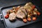 Traditional barbecue rolled lamb roast sliced with tomatoes and mini eggplant on a modern design black tray