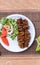 A traditional barbeque dish bihari kabab in a white plate along vegetables on a wooden table top view