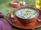 Traditional Bulgarian cold soup tarator with cucumber, herbs and walnuts in a brown clay bowl on a green concrete background. Cold