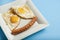 Traditional Clasic Breakfast Fried Eggs and Sausage on a white Square Porcelain Plate. Isoalted on Blue Background.
