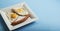 Traditional Clasic Breakfast Fried Eggs and Sausage on a white Square Porcelain Plate. Isoalted on Blue Background. Banner Copy Sp